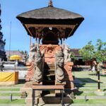 Hindu temple complex with an ornate central shrine & a leafy courtyard guarded by stone statues.