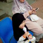 A tree-shaded path rings a lake in a park known for fountains that are vividly illuminated at night.